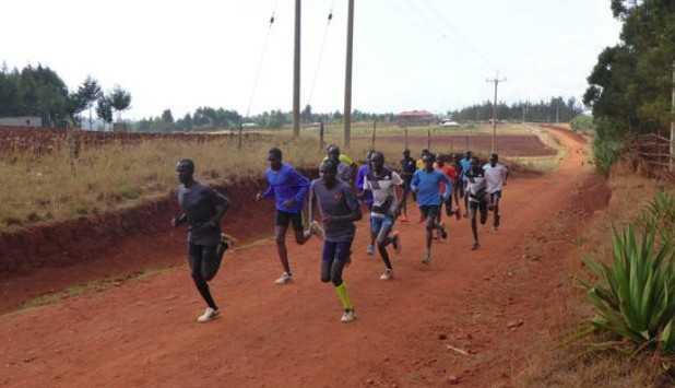 Grupo de candidatos/recrutas em treino de corrida (resistência) na Escola Prática da PRM em Matalane, Moçambique, numa estrada de terra.